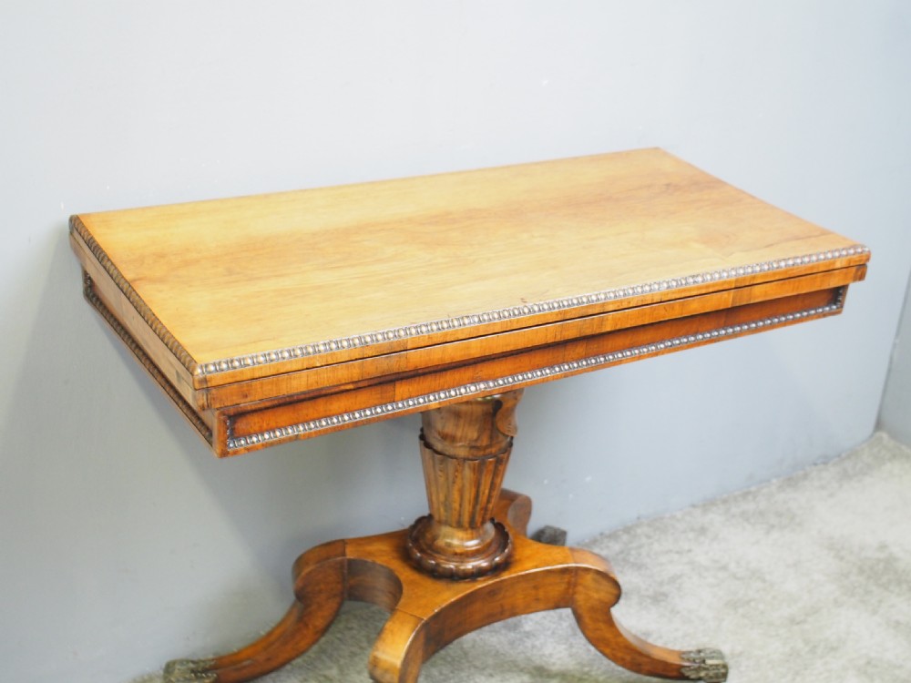 A George III rosewood games table featuring a beaded fold-over top, central turned pedestal support, and four splayed legs with brass castors. View III