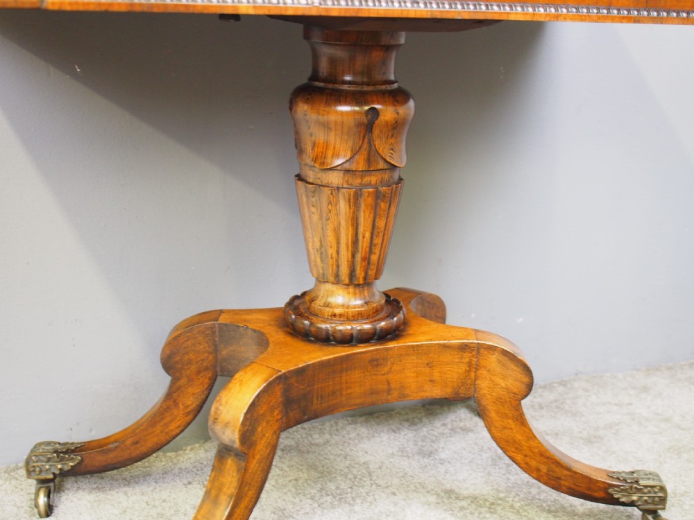 A George III rosewood games table featuring a beaded fold-over top, central turned pedestal support, and four splayed legs with brass castors. View VIII