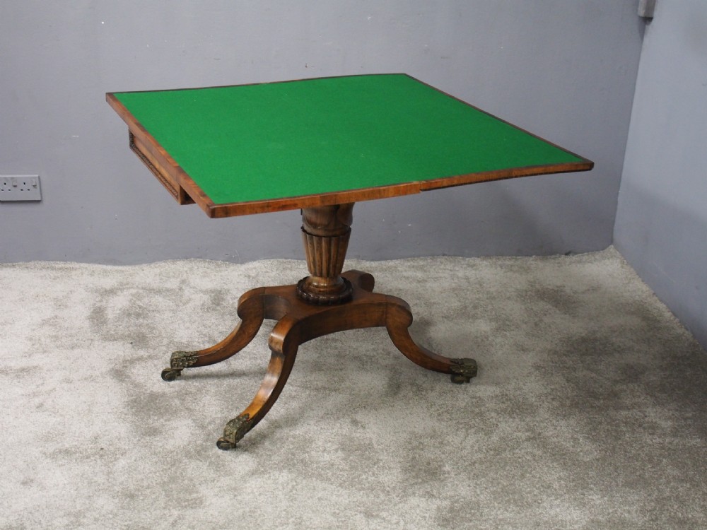 A George III rosewood games table featuring a beaded fold-over top, central turned pedestal support, and four splayed legs with brass castors. View X