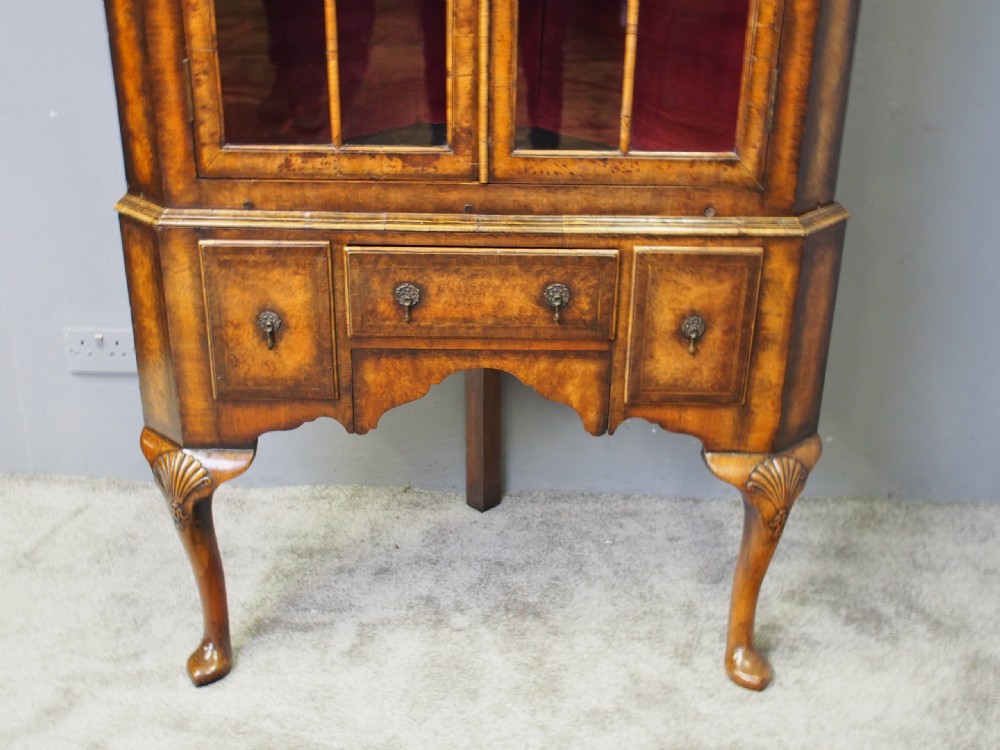 A standing George I style burr walnut corner cabinet featuring double glazed doors with arched upper panels, lower drawers, and carved cabriole legs. View VI