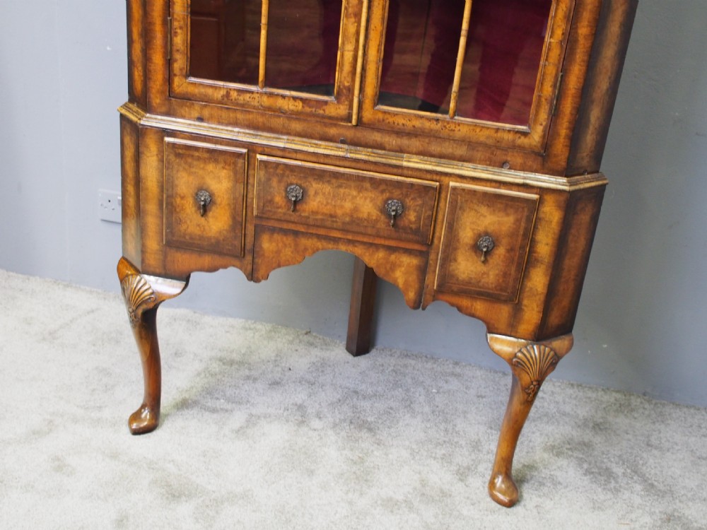 A standing George I style burr walnut corner cabinet featuring double glazed doors with arched upper panels, lower drawers, and carved cabriole legs. View VII