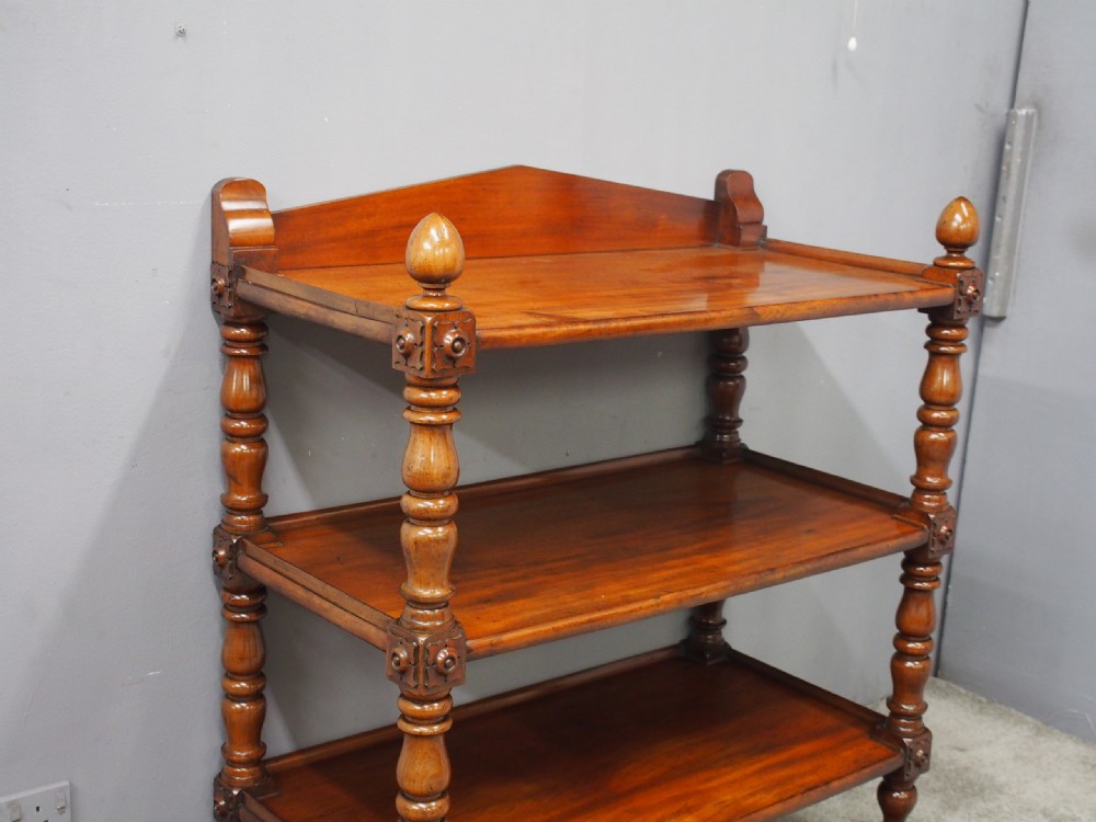 A William IV mahogany three-tier buffet featuring turned column supports, carved corner blocks, top finials, a low shaped gallery back, and brass castors. View III