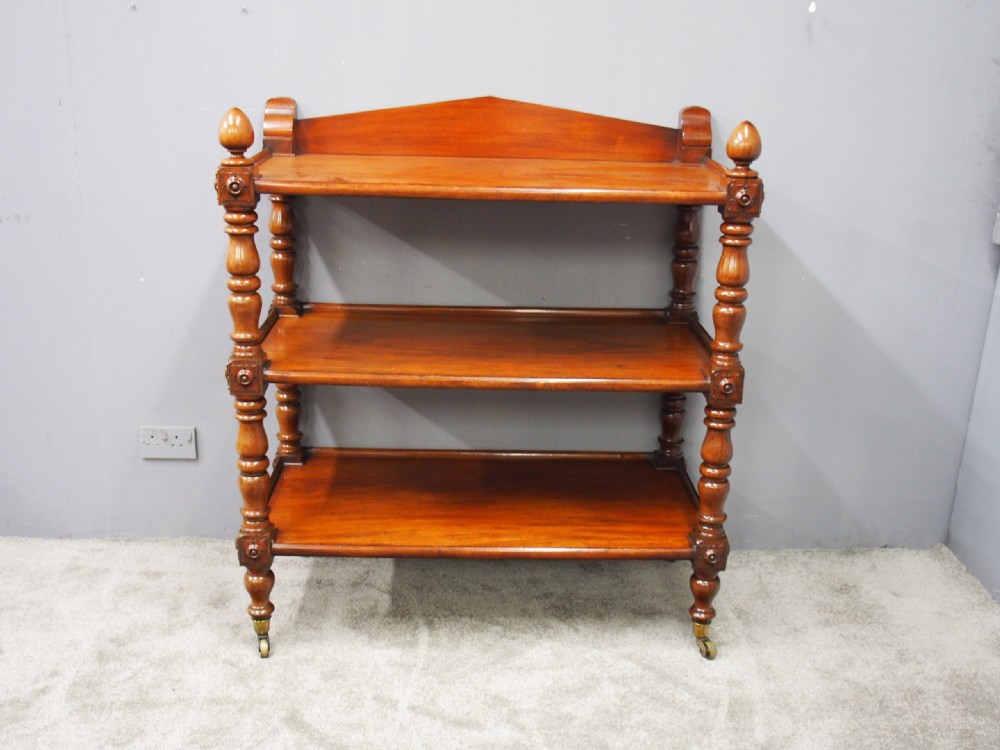 A William IV mahogany three-tier buffet featuring turned column supports, carved corner blocks, top finials, a low shaped gallery back, and brass castors. View VIII