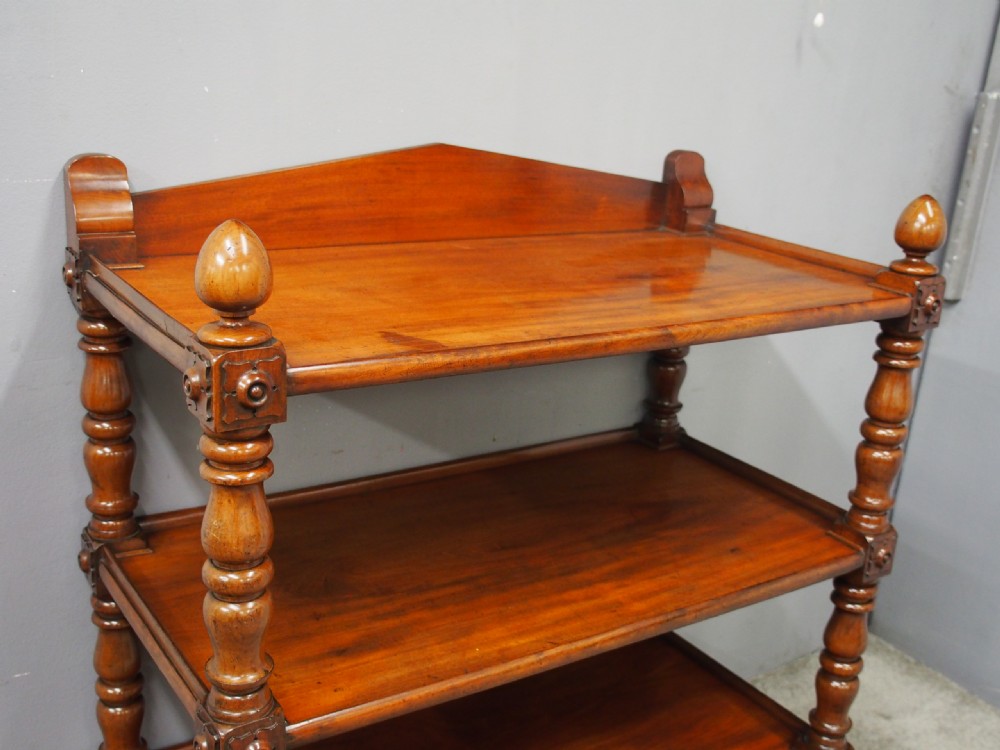 A William IV mahogany three-tier buffet featuring turned column supports, carved corner blocks, top finials, a low shaped gallery back, and brass castors. View IX