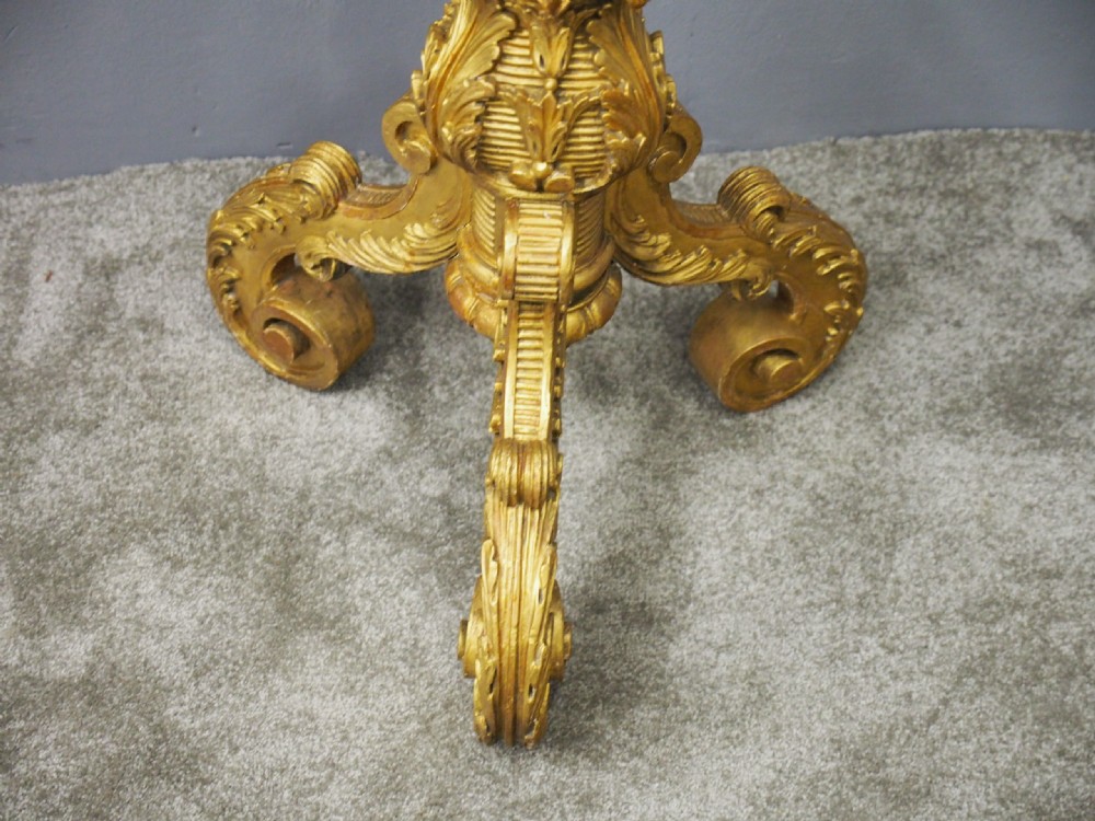 A tall Charles II style carved giltwood torchere stand with a circular top, baluster column decorated with foliage, and a tripod scroll base. View VIII