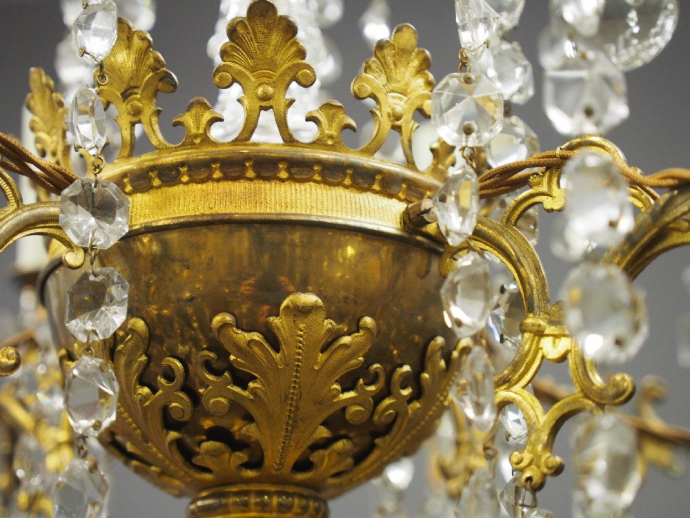 A two-tiered ceiling chandelier featuring a gilded brass frame adorned with multiple hanging glass prisms and six candle-style light sockets. View VII