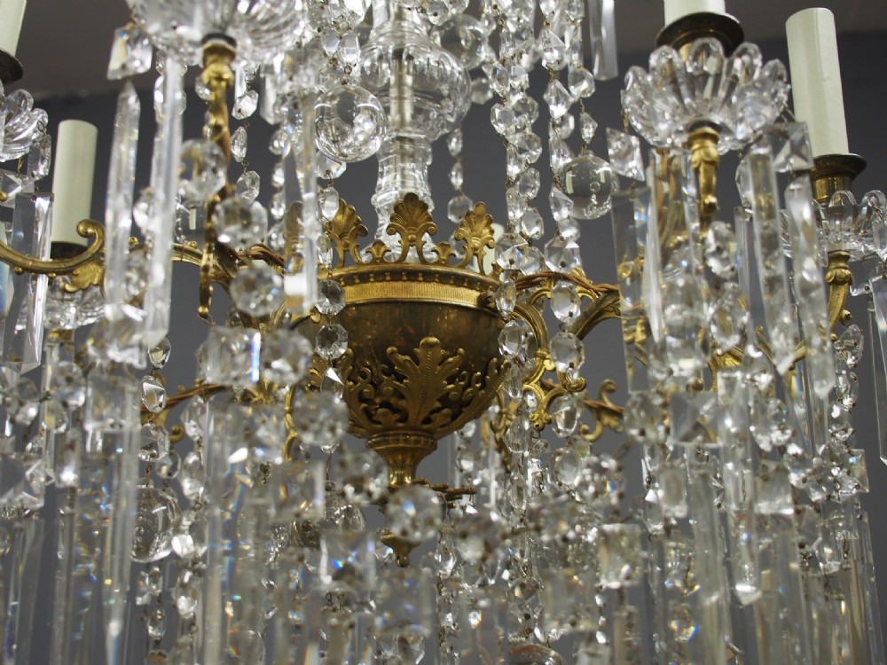 A two-tiered ceiling chandelier featuring a gilded brass frame adorned with multiple hanging glass prisms and six candle-style light sockets. View VIII