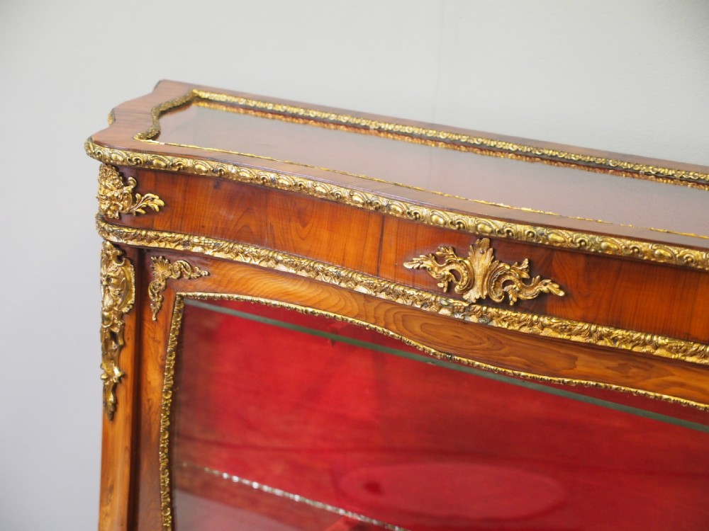 A Victorian yew wood vitrine display cabinet with gilt-bronze ormolu mounts, curved glass front, and red velvet lining. View IV