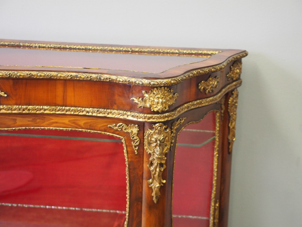 A Victorian yew wood vitrine display cabinet with gilt-bronze ormolu mounts, curved glass front, and red velvet lining. View V