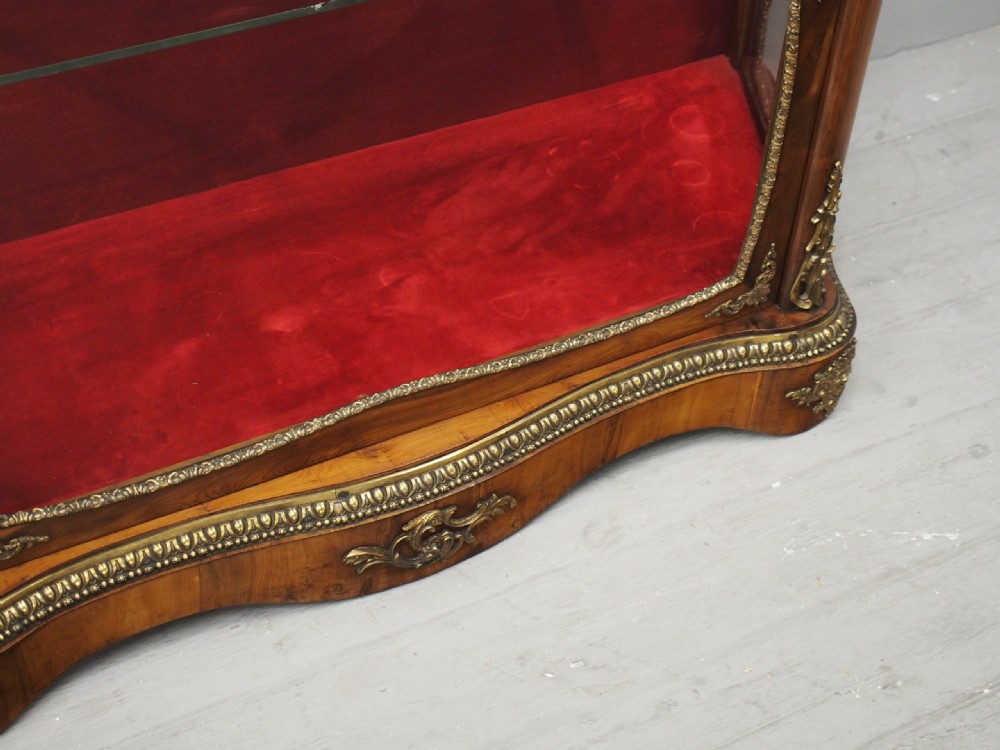 A Victorian yew wood vitrine display cabinet with gilt-bronze ormolu mounts, curved glass front, and red velvet lining. View IX