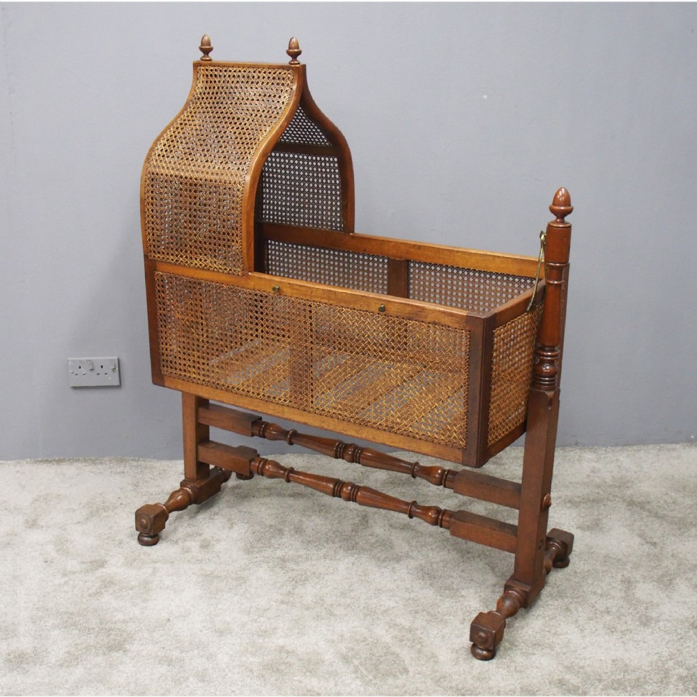A William IV mahogany and cane cradle featuring a curved hooded canopy, turned side supports, and acorn finials.