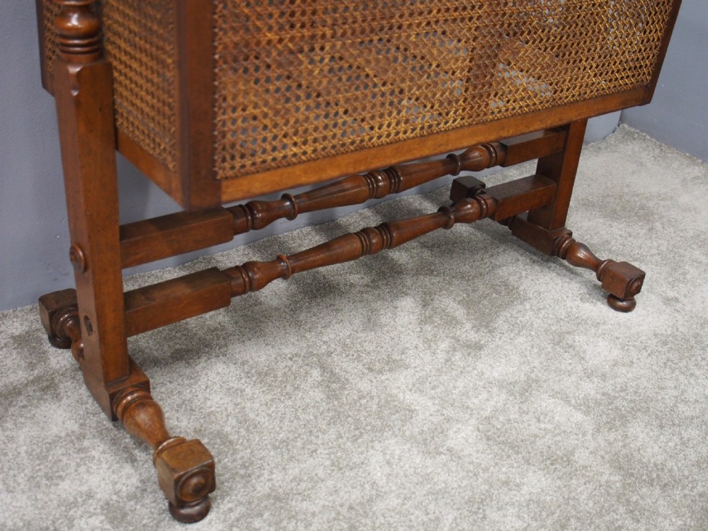 A William IV mahogany and cane cradle featuring a curved hooded canopy, turned side supports, and acorn finials. View VI