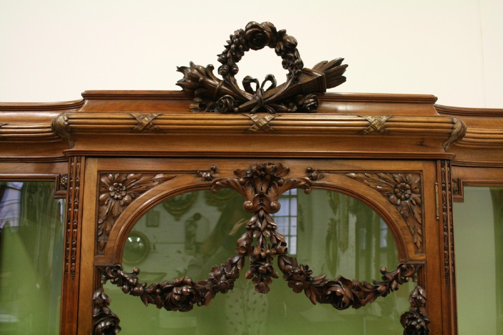 A carved walnut French display cabinet featuring glazed doors, glass shelves, green fabric interior lining, and turned fluted legs. View II