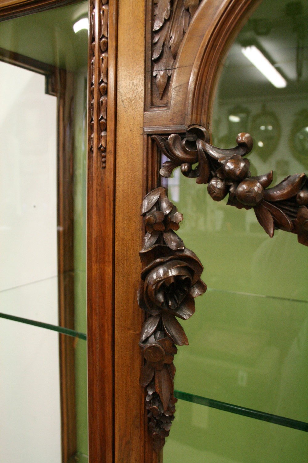 A carved walnut French display cabinet featuring glazed doors, glass shelves, green fabric interior lining, and turned fluted legs. View III