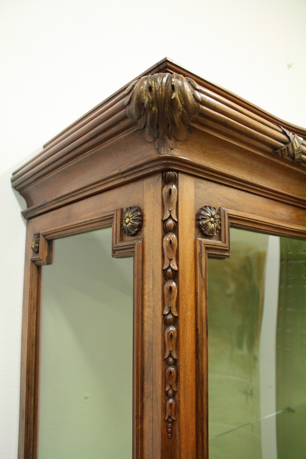 A carved walnut French display cabinet featuring glazed doors, glass shelves, green fabric interior lining, and turned fluted legs. View VI