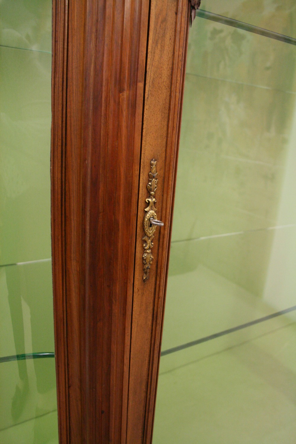 A carved walnut French display cabinet featuring glazed doors, glass shelves, green fabric interior lining, and turned fluted legs. View VII