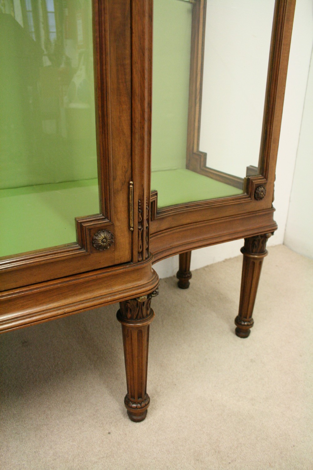 A carved walnut French display cabinet featuring glazed doors, glass shelves, green fabric interior lining, and turned fluted legs. View VIII