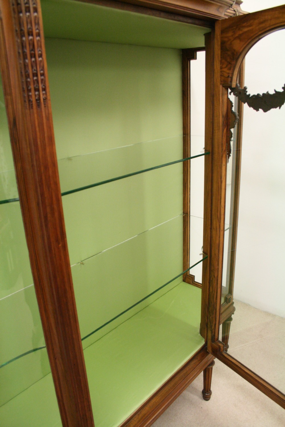 A carved walnut French display cabinet featuring glazed doors, glass shelves, green fabric interior lining, and turned fluted legs. View IX