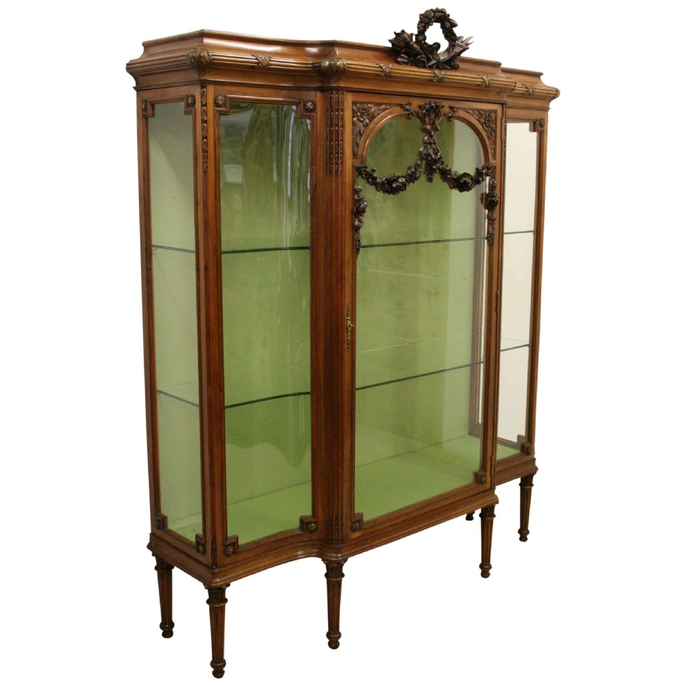 A carved walnut French display cabinet featuring glazed doors, glass shelves, green fabric interior lining, and turned fluted legs. View X
