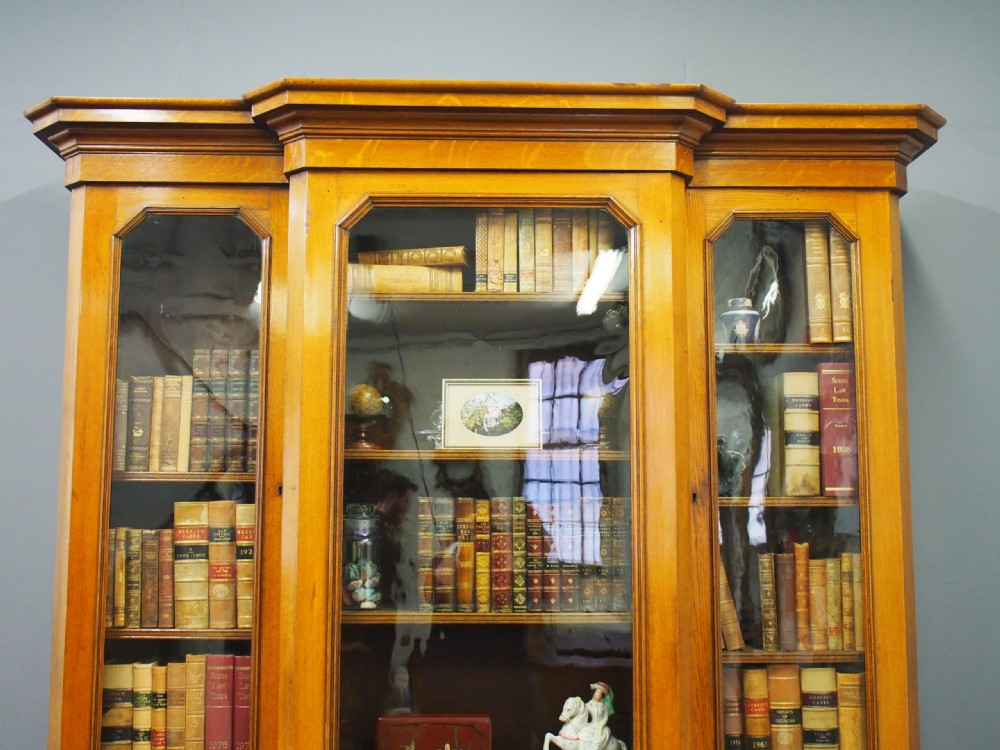 A Victorian golden oak breakfront bookcase featuring three arch-glazed upper doors above three solid timber panel cupboard doors. View V