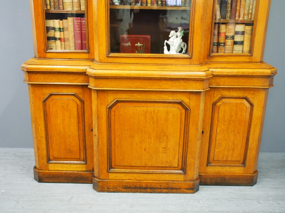 A Victorian golden oak breakfront bookcase featuring three arch-glazed upper doors above three solid timber panel cupboard doors. View VI