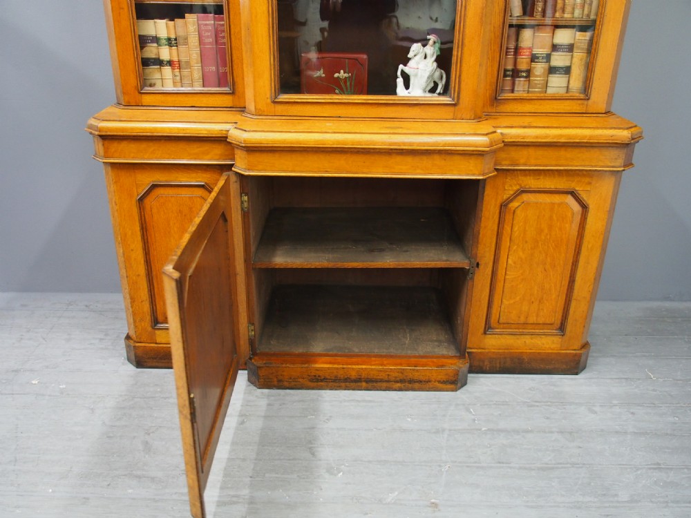A Victorian golden oak breakfront bookcase featuring three arch-glazed upper doors above three solid timber panel cupboard doors. View IX