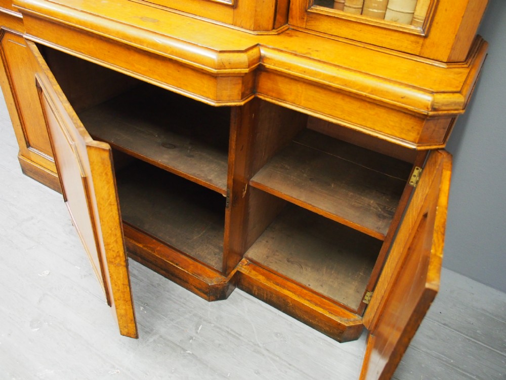 A Victorian golden oak breakfront bookcase featuring three arch-glazed upper doors above three solid timber panel cupboard doors. View X