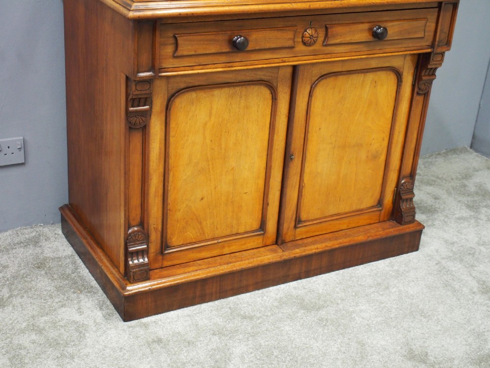 A mid-Victorian mahogany glazed bookcase cabinet with two glass upper doors above a two-door solid cupboard base with carved details. View IV
