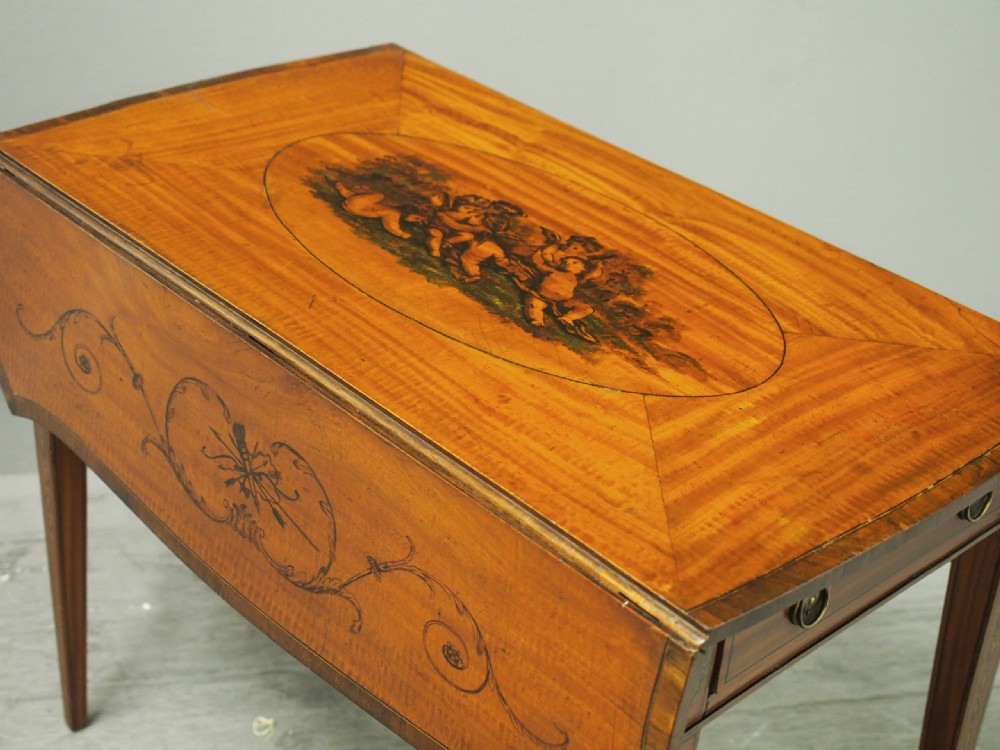 A George III painted satinwood Pembroke table featuring two drop-down leaves, a central oval vignette painting, floral detail, a frieze drawer, and square tapered legs. View VII