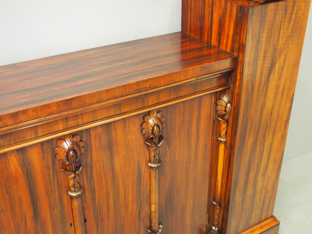 A Regency period goncalo alves wood cabinet featuring two outer pedestal towers and carved leaf motif pilasters along the central panel. View X