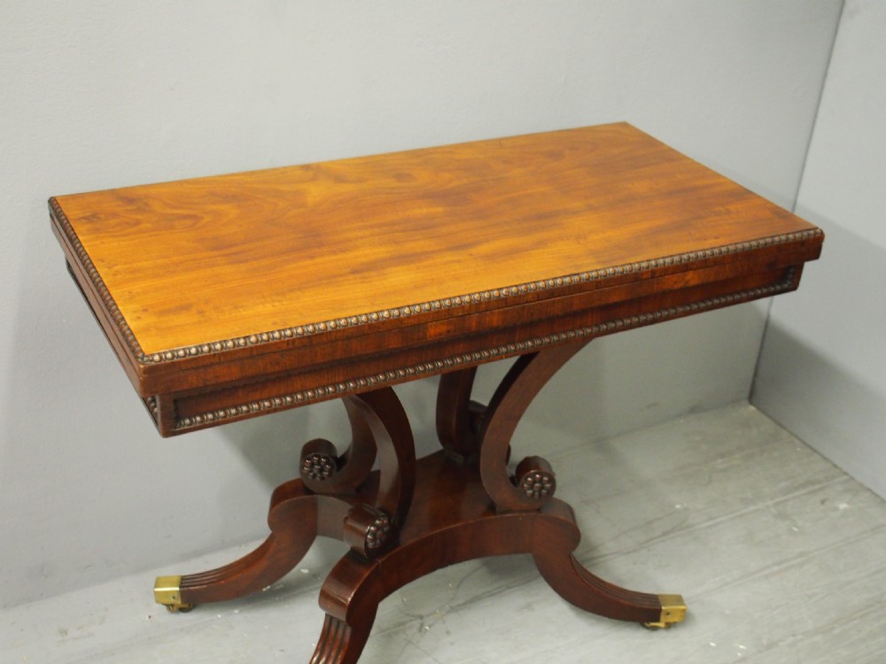 A Regency mahogany fold-over tea table featuring bead moulding along the frieze, set on scrolled supports and reeded splayed legs with brass castors. View III
