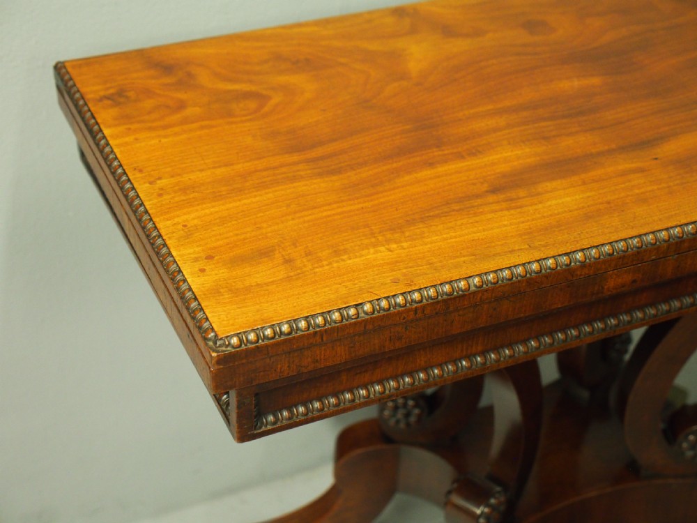 A Regency mahogany fold-over tea table featuring bead moulding along the frieze, set on scrolled supports and reeded splayed legs with brass castors. View IV