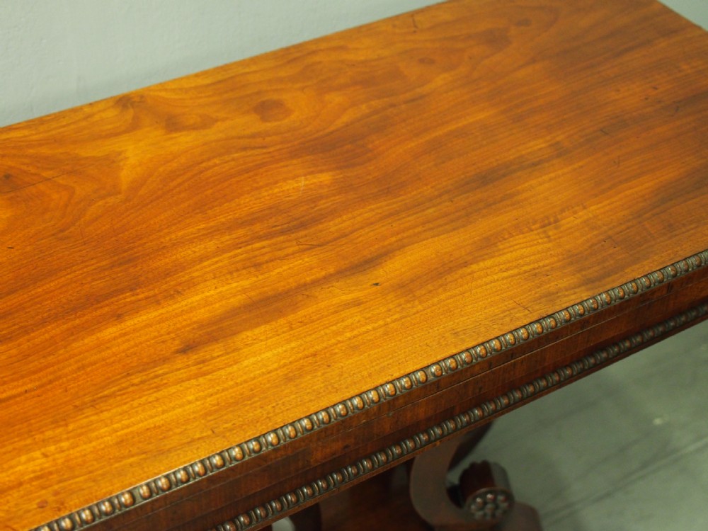 A Regency mahogany fold-over tea table featuring bead moulding along the frieze, set on scrolled supports and reeded splayed legs with brass castors. View V