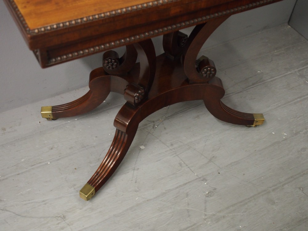 A Regency mahogany fold-over tea table featuring bead moulding along the frieze, set on scrolled supports and reeded splayed legs with brass castors. View VI