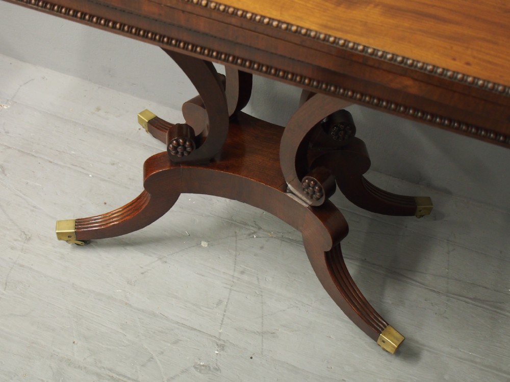 A Regency mahogany fold-over tea table featuring bead moulding along the frieze, set on scrolled supports and reeded splayed legs with brass castors. View VII