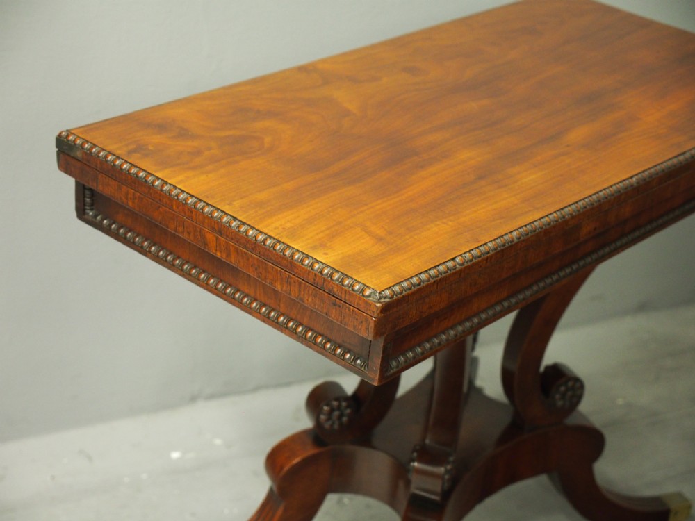 A Regency mahogany fold-over tea table featuring bead moulding along the frieze, set on scrolled supports and reeded splayed legs with brass castors. View IX