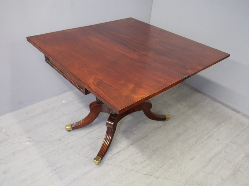 A Regency mahogany fold-over tea table featuring bead moulding along the frieze, set on scrolled supports and reeded splayed legs with brass castors. View XIII