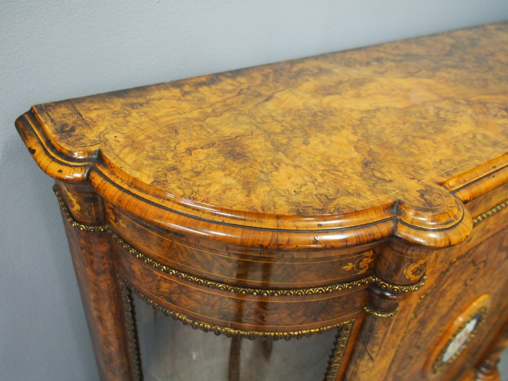 Victorian burr walnut credenza featuring a central door with marquetry inlay and a porcelain medallion, flanked by two curved glazed side cabinets with gilt mounts. View VII
