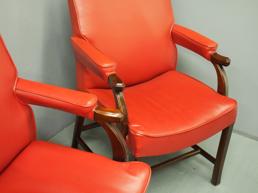 A pair of red leather armchairs with dark mahogany frames and padded armrests. View X