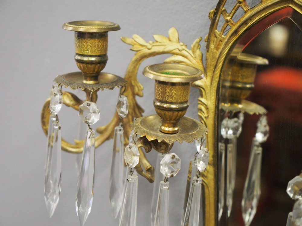 A pair of ornate French Neoclassical ormolu wall sconces featuring oval mirrored backs, multi-arm candleholders, cut crystal prisms, and top trophy crests. View VI
