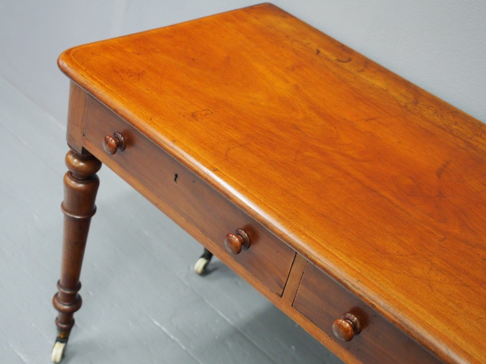 Victorian mahogany side table featuring two frieze drawers with wooden knob handles, turned legs, and white ceramic castors. View VI