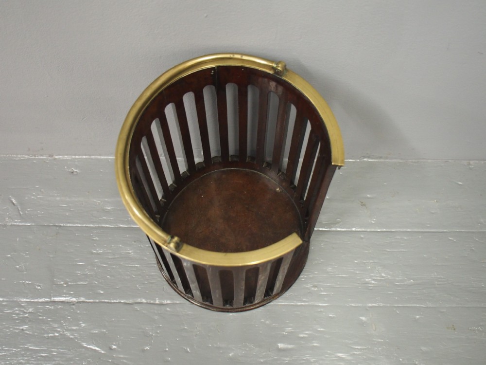 A cylindrical George III dark mahogany plate bucket with vertical cutout slats, a side slot, a brass upper rim, and a movable brass swing handle. View IV