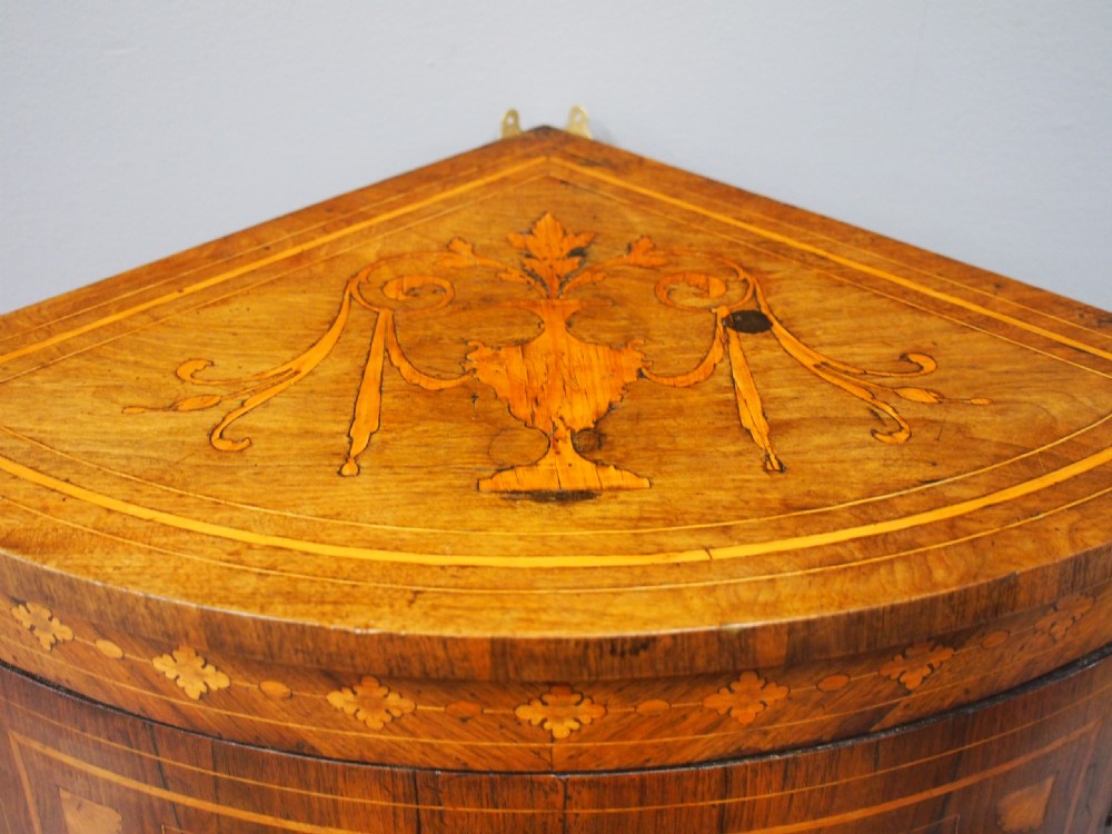 A floor-standing Dutch walnut corner cabinet featuring a curved front door embellished with figurative and floral marquetry inlays resting on carved legs. View VII