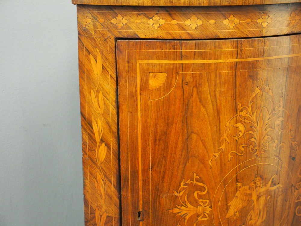 A floor-standing Dutch walnut corner cabinet featuring a curved front door embellished with figurative and floral marquetry inlays resting on carved legs. View X