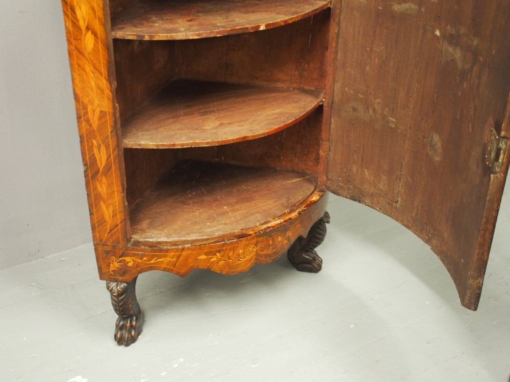 A floor-standing Dutch walnut corner cabinet featuring a curved front door embellished with figurative and floral marquetry inlays resting on carved legs. View XVI