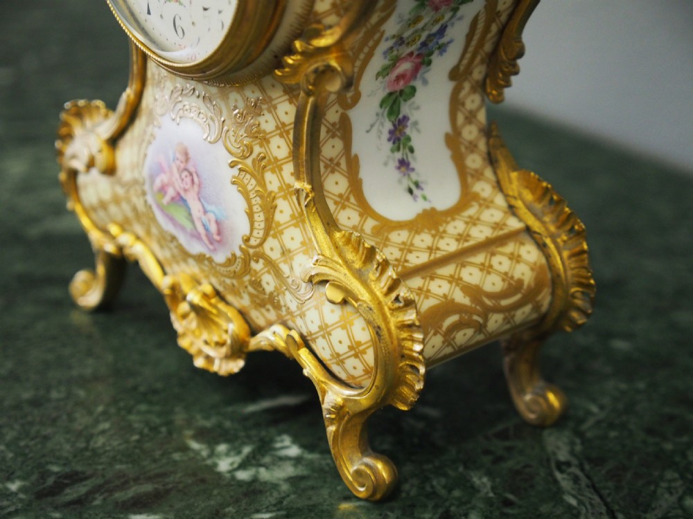 A three-piece French porcelain clock garniture set featuring a central rococo-style clock flanked by two matching vases decorated with hand-painted cherubs and gilded mounts. View XIII