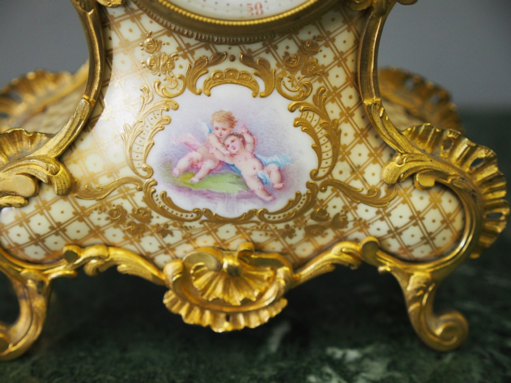 A three-piece French porcelain clock garniture set featuring a central rococo-style clock flanked by two matching vases decorated with hand-painted cherubs and gilded mounts. View XIV