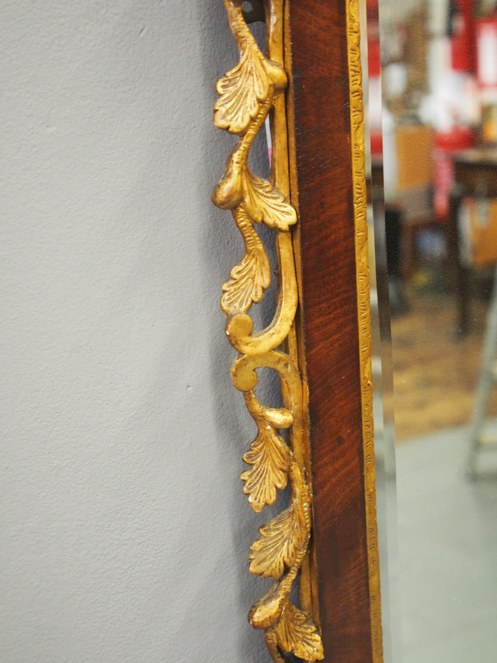 A vertical Chippendale style mahogany wall mirror featuring detailed giltwood foliage carvings along the side margins and top cresting, set against a dark timber frame with fretwork edges. View V