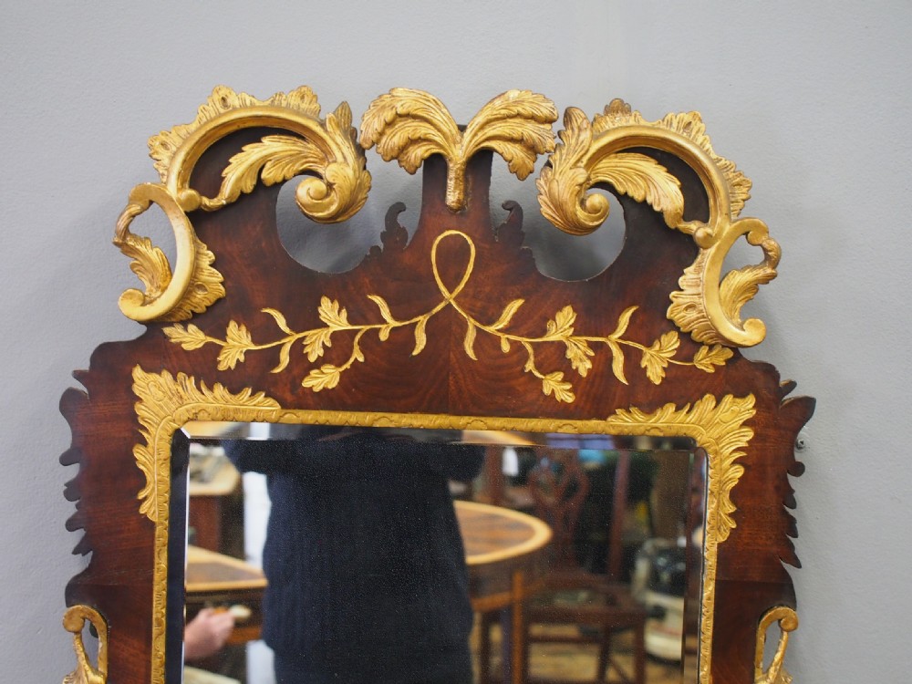 A vertical Chippendale style mahogany wall mirror featuring detailed giltwood foliage carvings along the side margins and top cresting, set against a dark timber frame with fretwork edges. View VIII