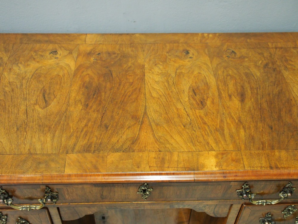A George II style walnut kneehole desk featuring figured wood veneers, a central cupboard in the recessed kneehole, multi-drawer storage with brass backplate handles, and bracket feet. View II